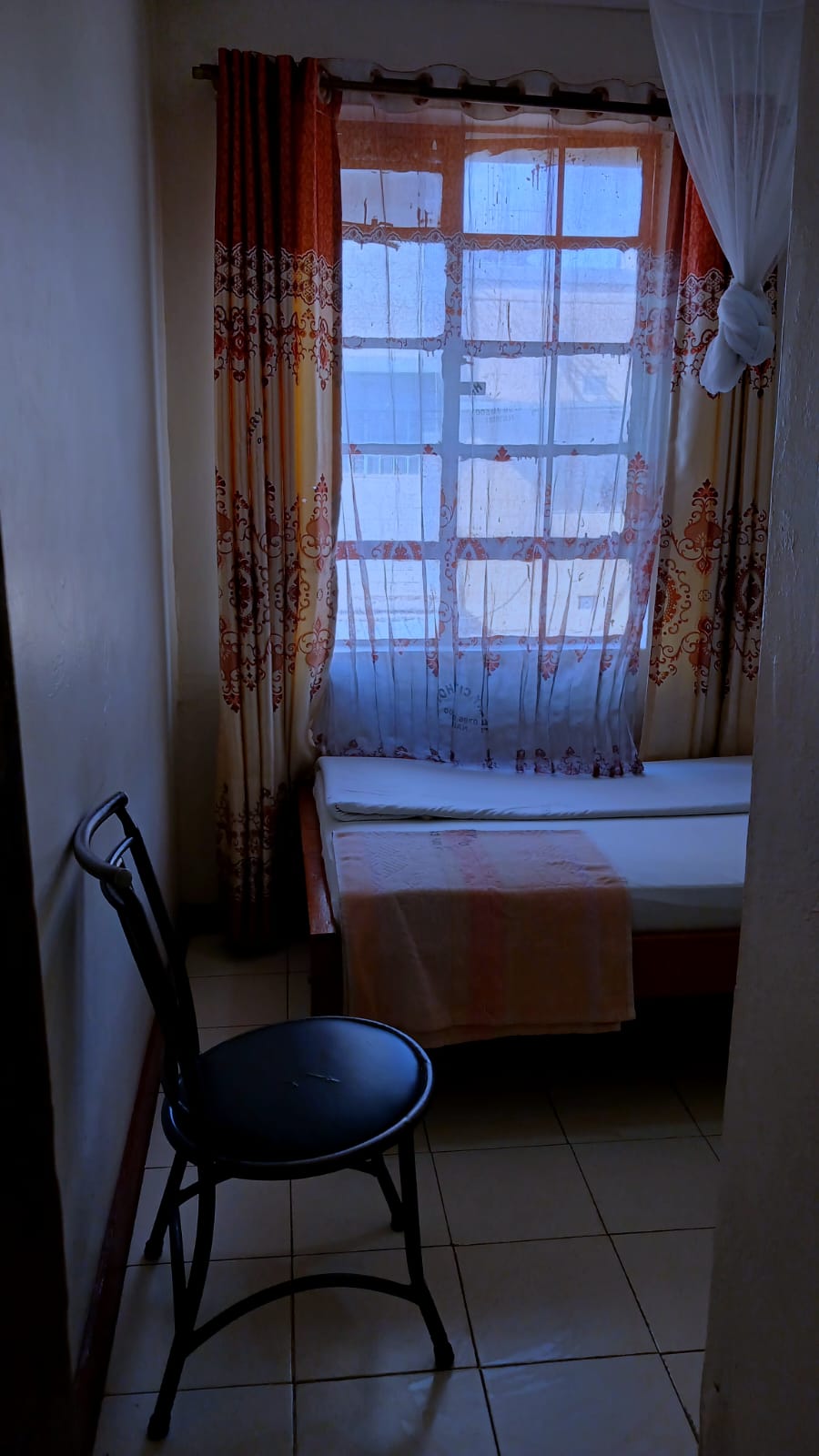 The Single Room — city-facing window with sheer curtains